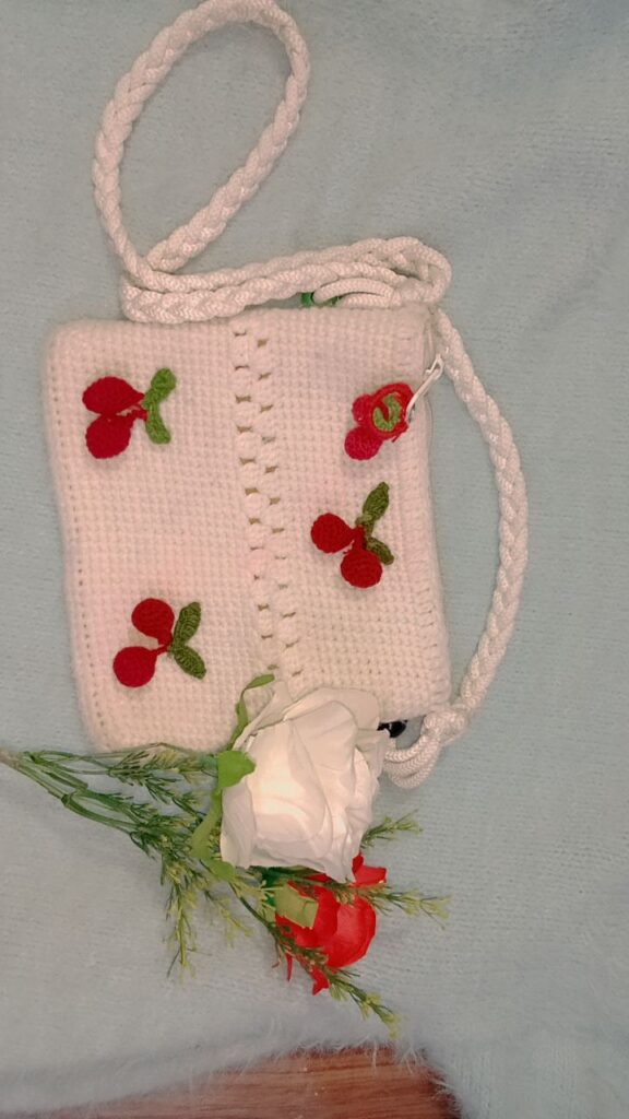 White sling bag with red cherries on the front flap and a long side strap for using it as crossbody bag.