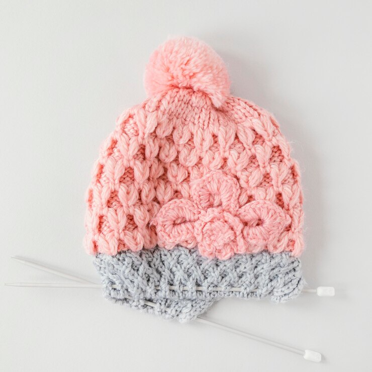 Unique handmade crochet women's beanie in pink and grey with a pom-pom and flower design, showcasing stylish crochet accessories.